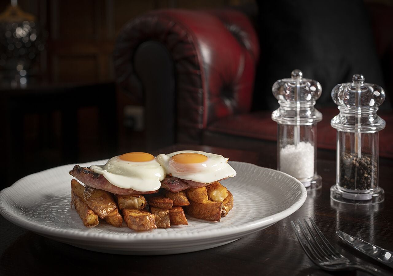 A plate of food with eggs and potatoes, salt and pepper shakers, and a fork and knife on a table.