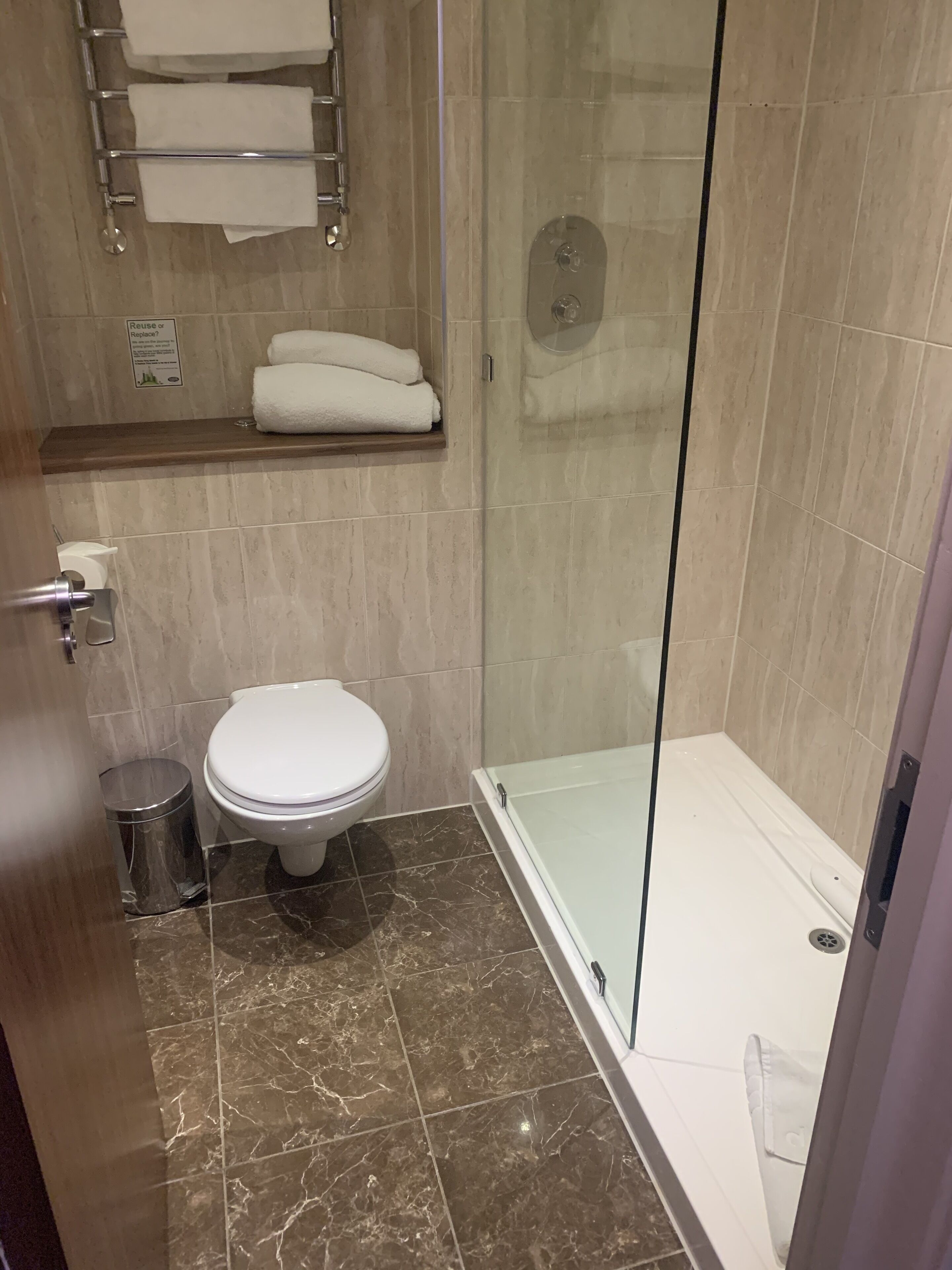 Un baño con inodoro, ducha envuelta en vidrio y piso de mármol.