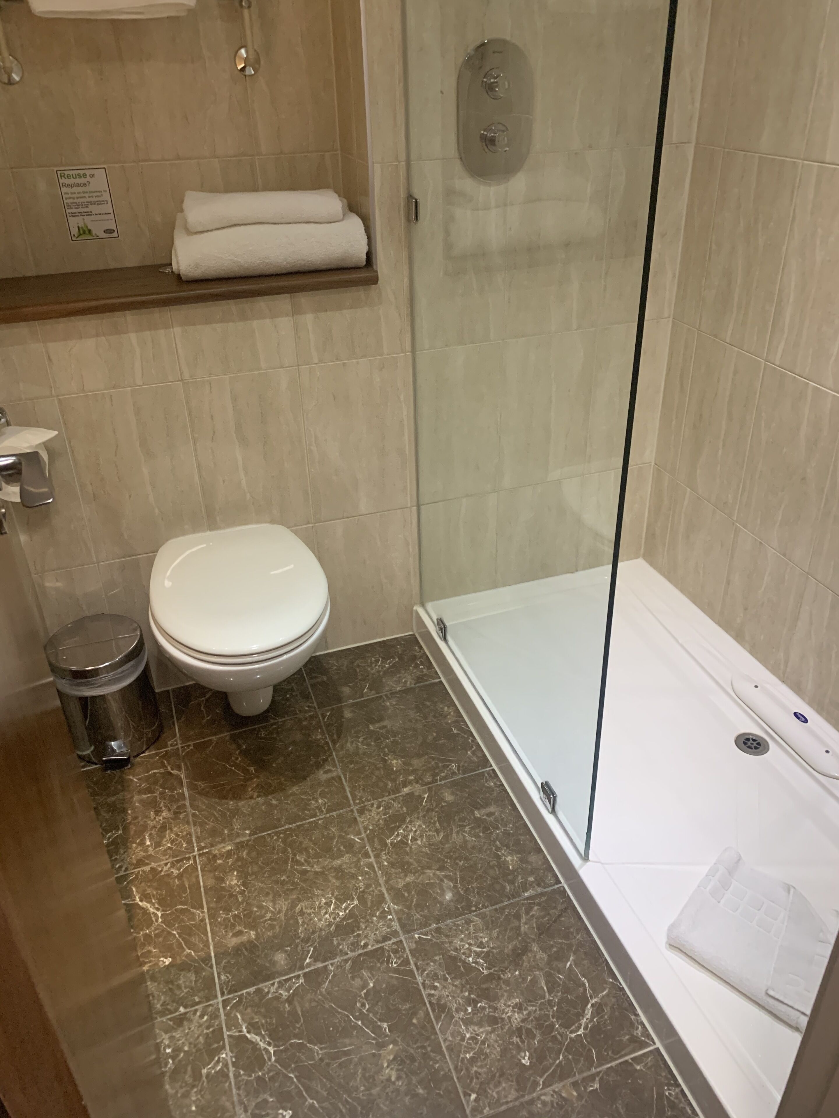 Un baño con inodoro, ducha envuelta en vidrio y suelo de mármol.