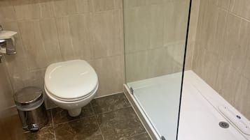 Un baño con inodoro, ducha envuelta en vidrio y suelo de mármol.