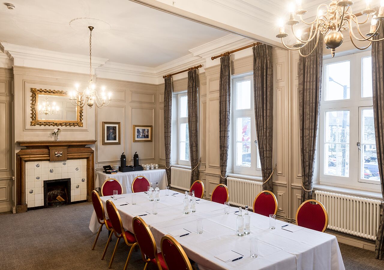 A conference room with a long table, red chairs, and a fireplace.