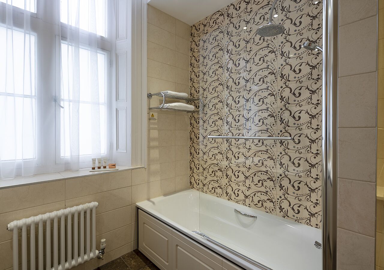 Un bagno con una vasca, una finestra con tende leggere, una doccia e piastrelle decorate.