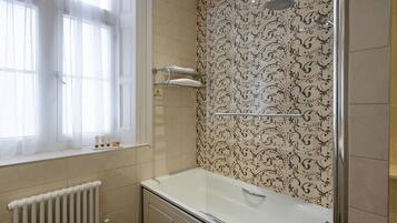 Un bagno con una vasca, una finestra con tende leggere, una doccia e piastrelle decorate.