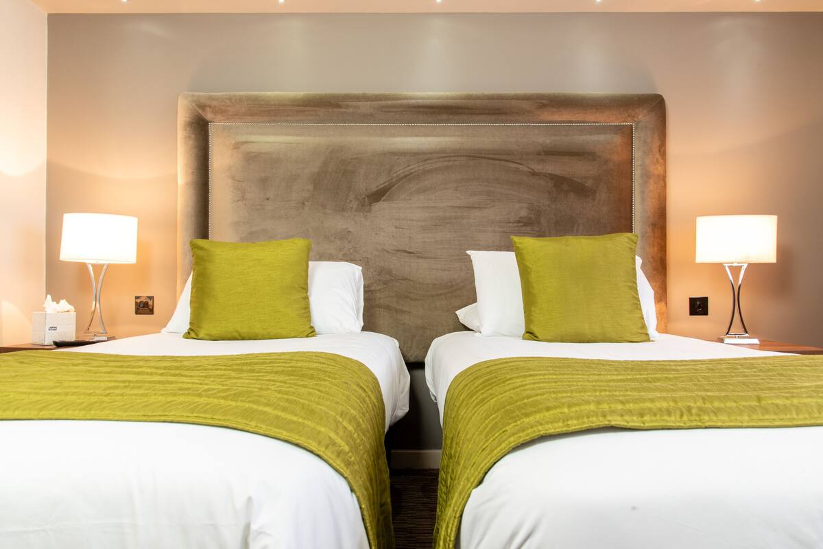 Ein Hotelzimmer mit zwei Betten, jeweils mit grün-weißer Bettwäsche und einem großen hölzernen Kopfteil.