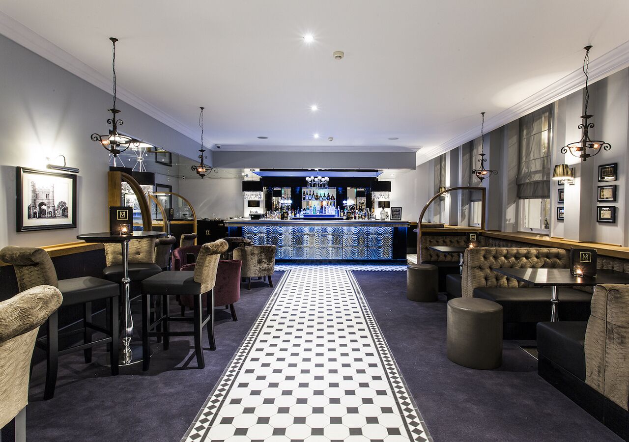 A bar area with a checkered floor, bar stools, and a bar counter with bottles.