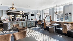 Un área de bar moderna con suelo estampado, arreglos de asientos y vistas amplias por ventanas grandes.
