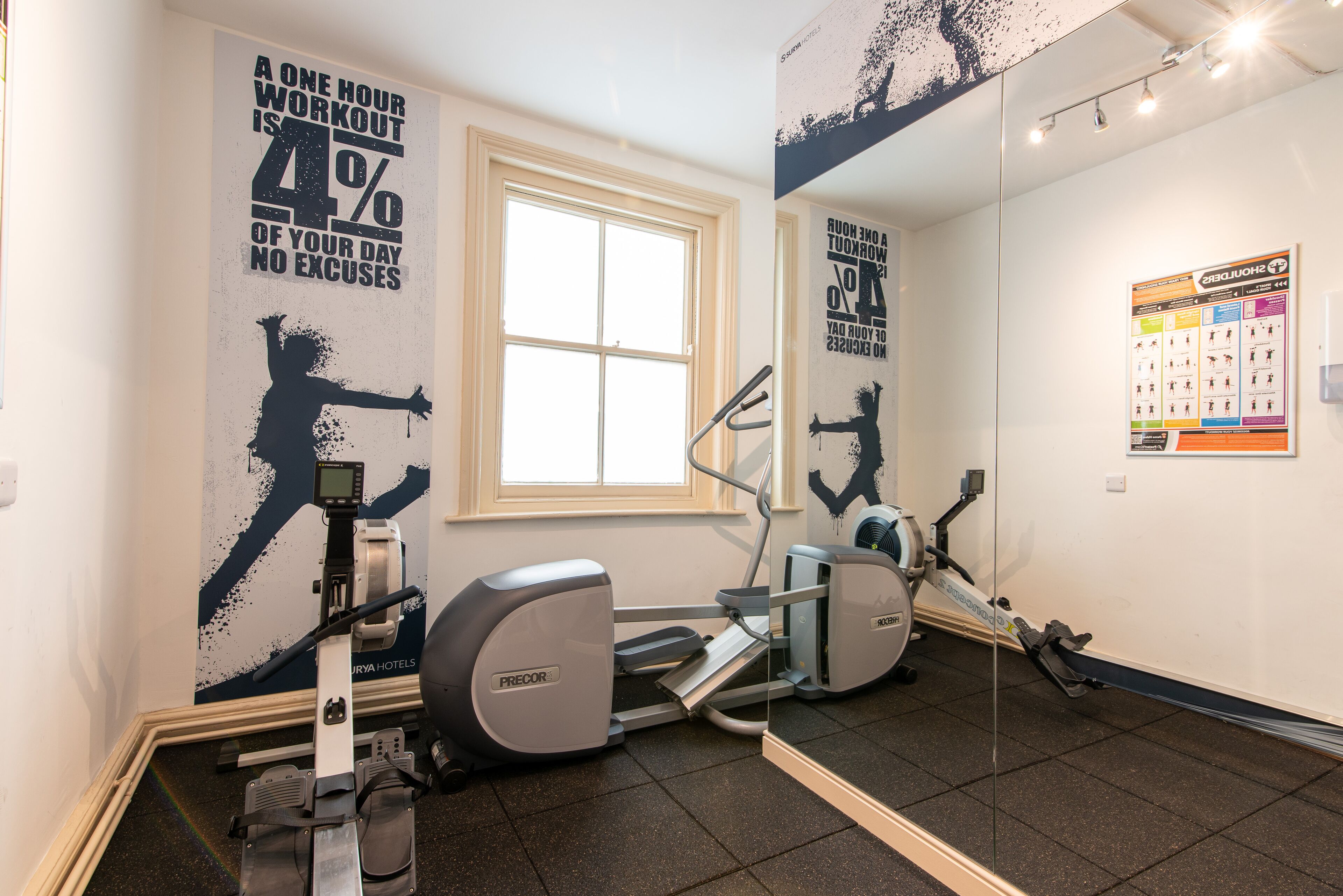 Une salle de sport équipée de machines de cardio, ornée d’affiches motivantes et dotée d’une fenêtre.