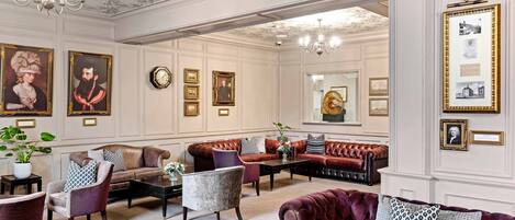 A spacious lounge with multiple seating areas, including sofas and armchairs, arranged around a central coffee table.