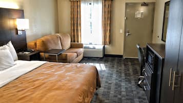 A hotel room with a bed, a sofa, a desk, a television, and a door.