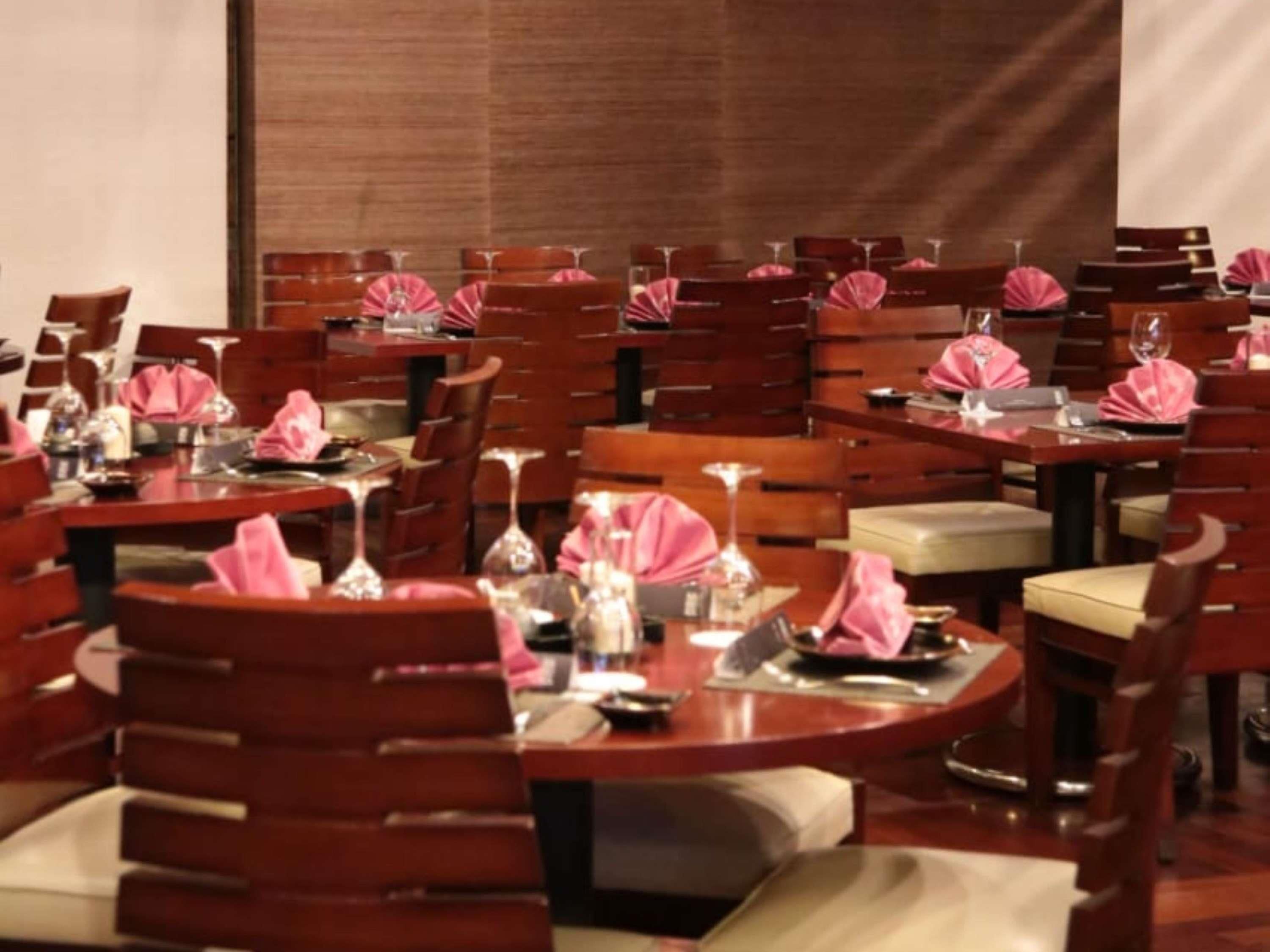 A hotel dining area with round tables, chairs, and pink tablecloths.