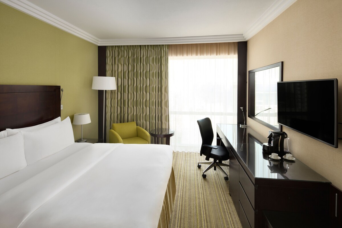 Une chambre d’hôtel avec un grand lit, un bureau doté d’un téléviseur à écran plat, une chaise et une fenêtre avec des rideaux.