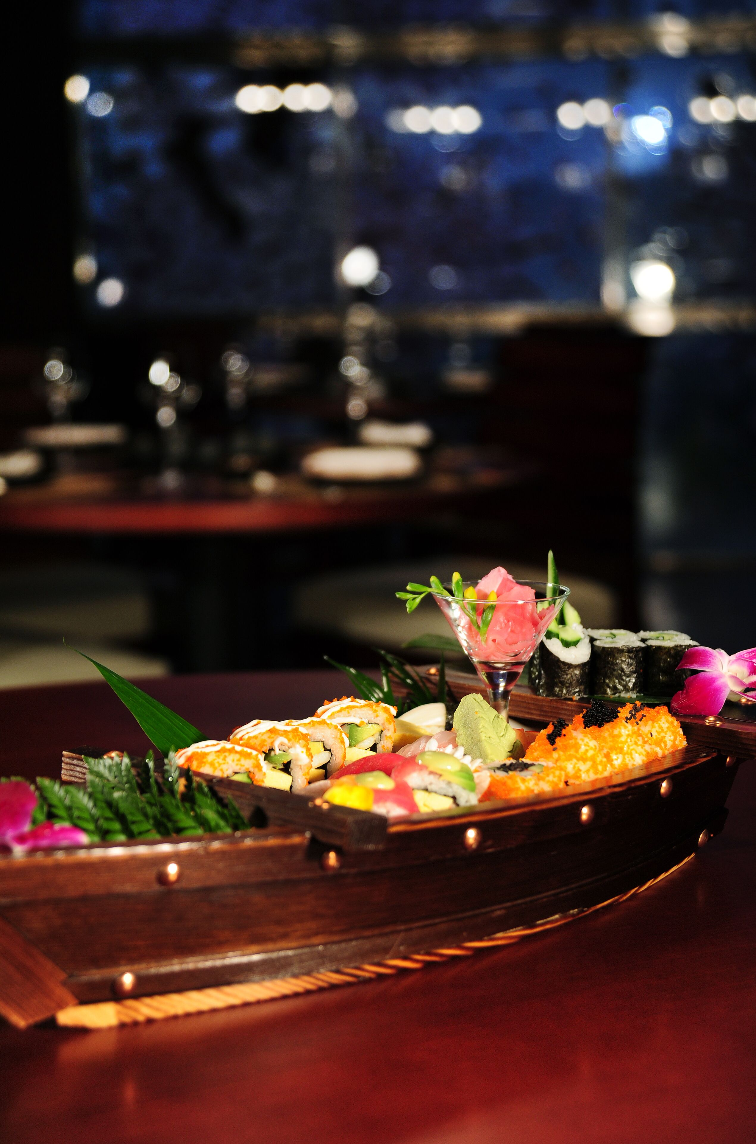 Una bandeja de sushi con diferentes tipos de sushi y un vaso de agua sobre una mesa de madera en un restaurante.