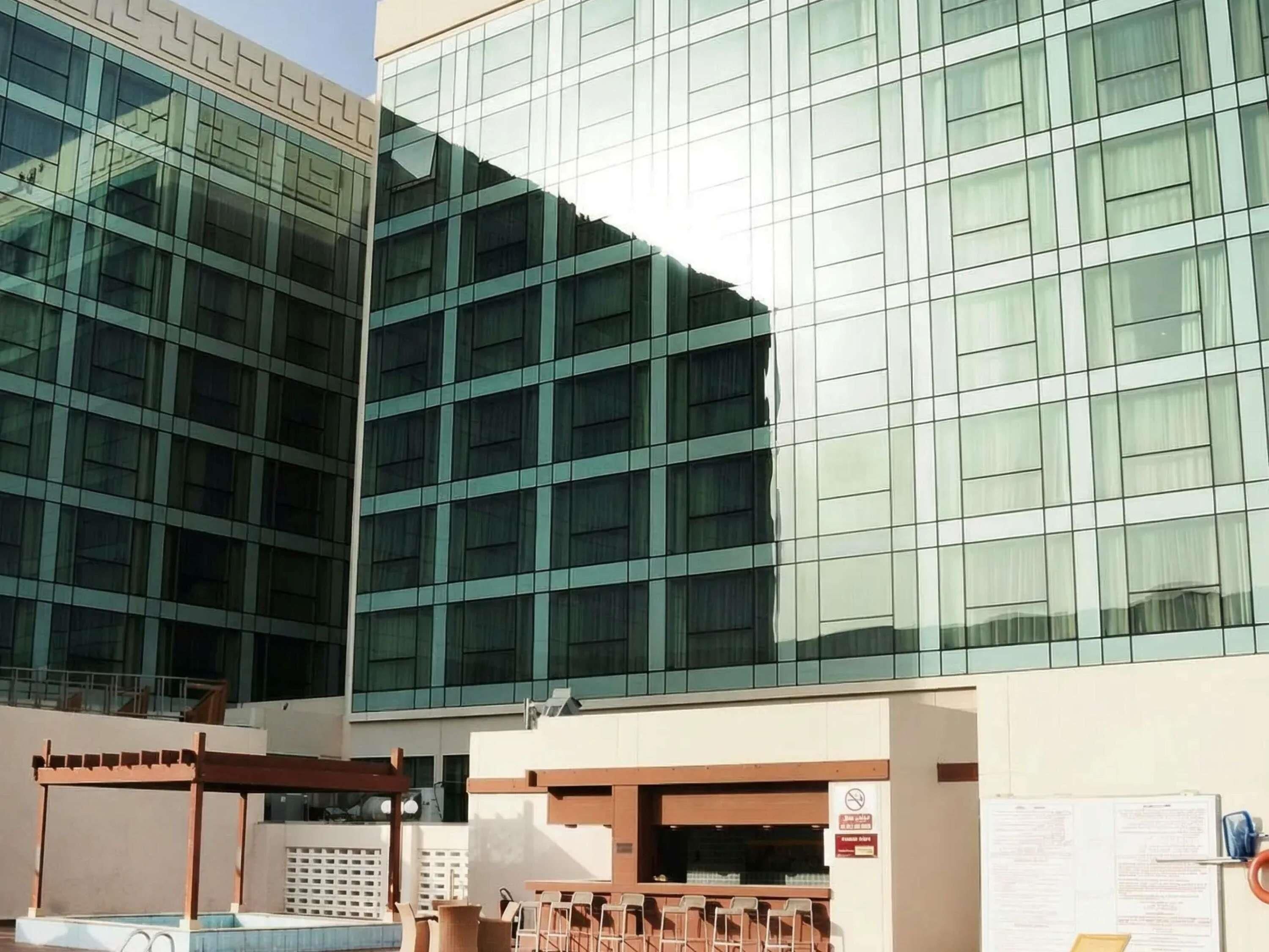 A modern building with a glass facade and a covered outdoor seating area with chairs.