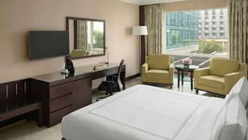 A hotel room with a bed, a desk, two chairs, a TV, and a window with a view of buildings.