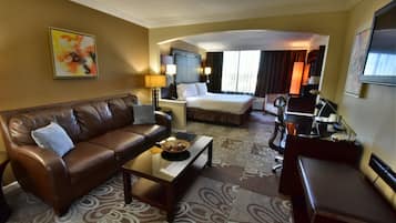 Habitación de hotel con sofá de cuero marrón, cama con ropa blanca, una mesita con una cesta y un escritorio con silla.