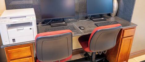 Un espace de travail équipé de deux écrans, d’une imprimante et de chaises de bureau.