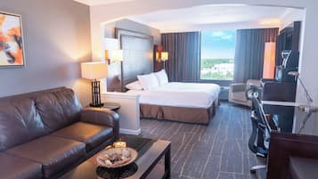 A hotel room with a sofa, a bed, a desk, a coffee machine, and a view of the outdoors.