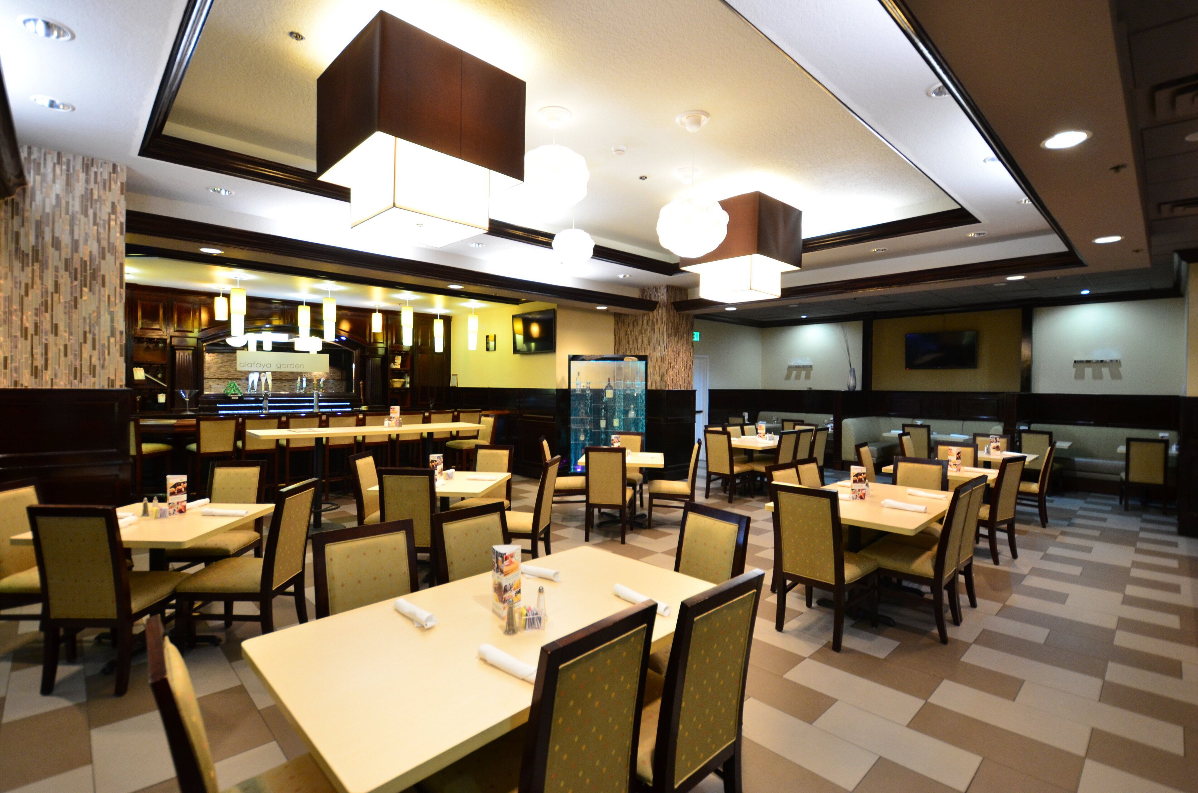 A restaurant with multiple tables and chairs, a bar area, and a wall-mounted television.