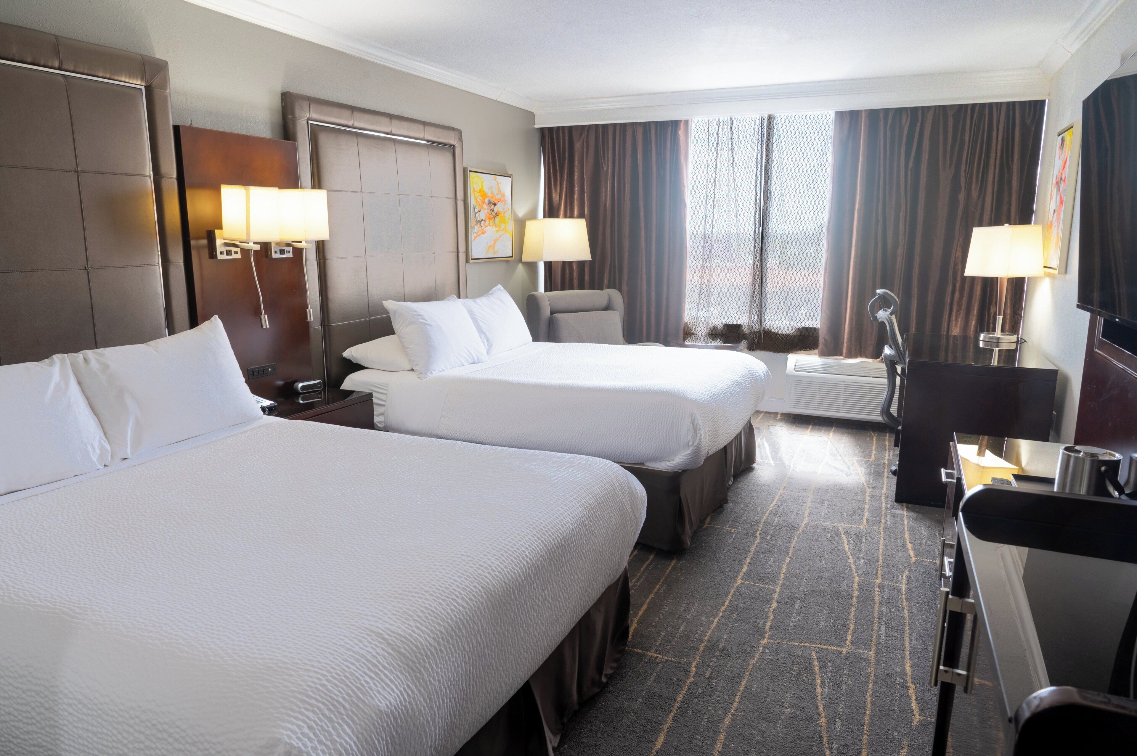 A hotel room with two beds, a desk, a chair, a TV, and a window with curtains.