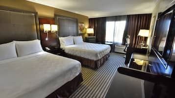 Ein Hotelzimmer mit zwei Betten, einem Schreibtisch, einem Stuhl, einem Fernseher und einem Fenster mit Vorhängen.