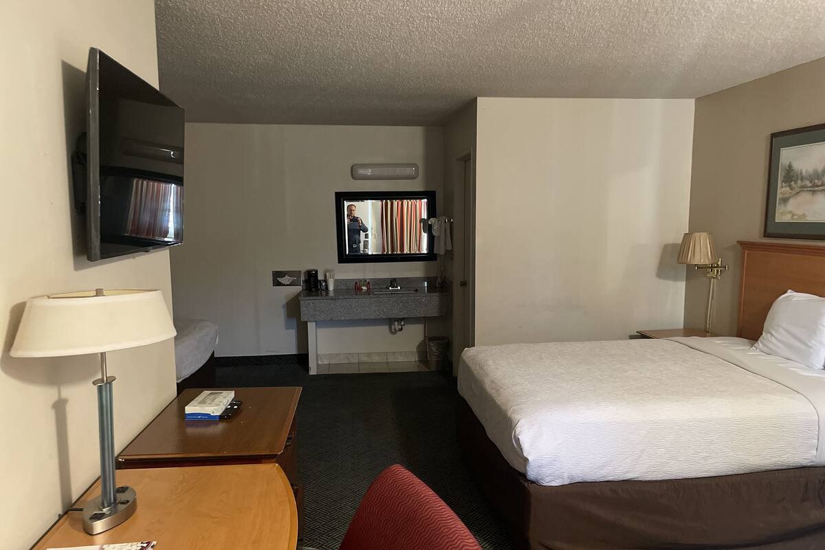 A hotel room with a bed, a desk, a TV, a mirror, and a bathroom.