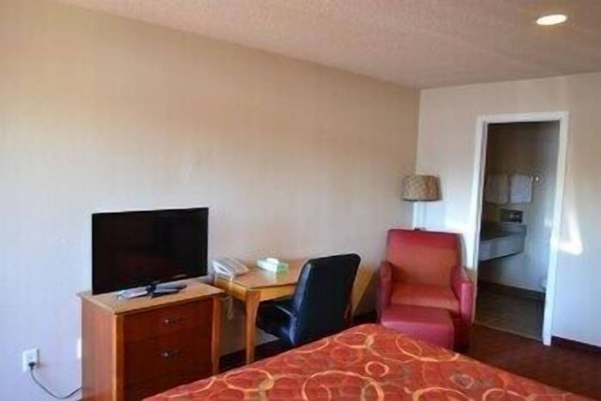 A hotel room with a bed, a desk with a chair, a television, and a lamp.