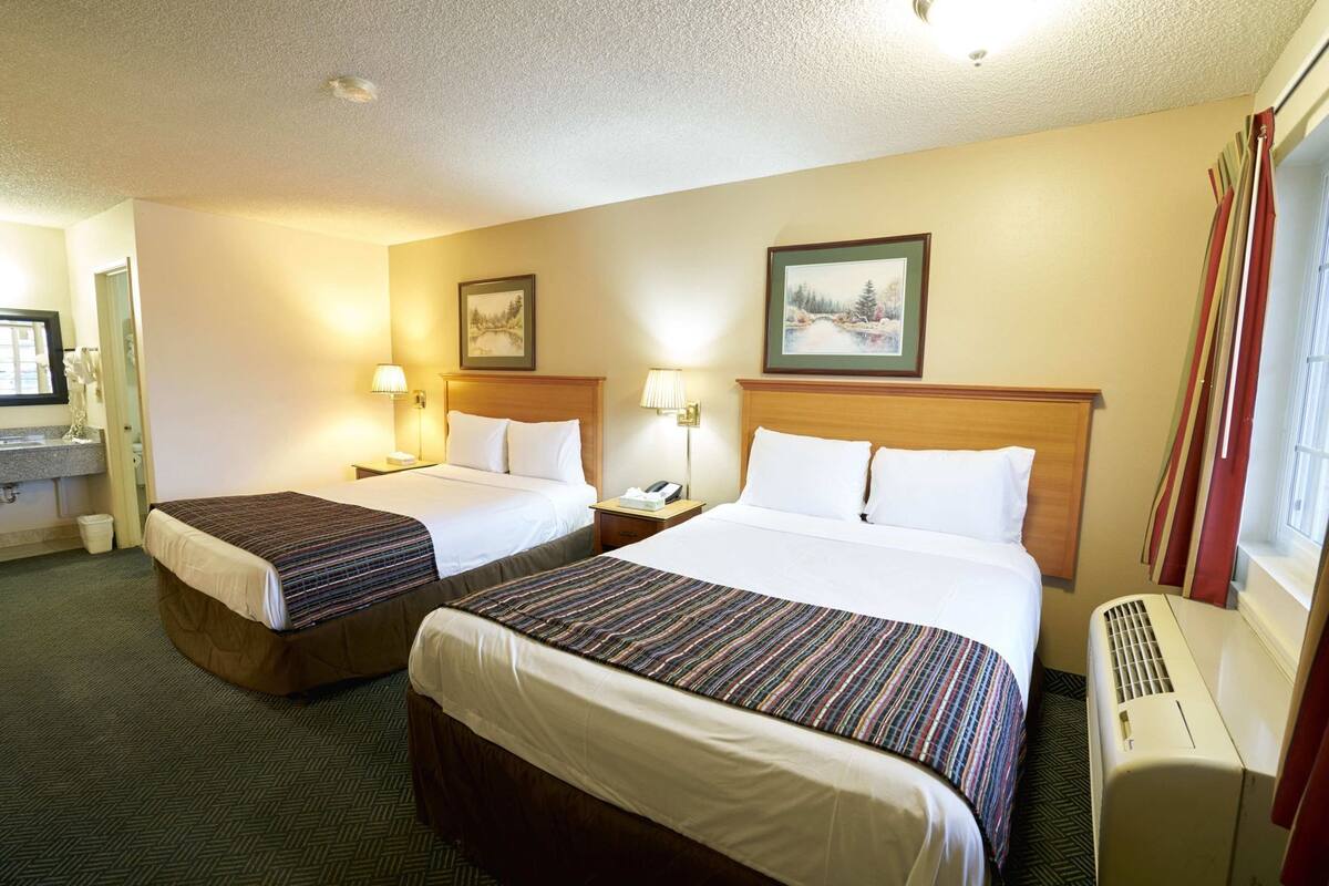 A hotel room with two beds, a desk with a telephone, and a window with curtains.
