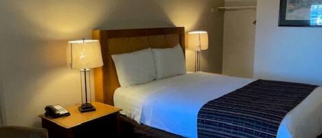 A hotel room with a bed, two bedside lamps, a nightstand with a phone, and a chair.