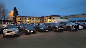 A parking lot with multiple cars parked in front of a building with a red roof and multiple windows.