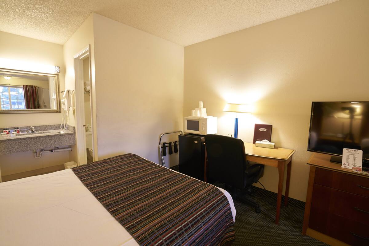 A hotel room with a bed, a desk with a computer, a television, and a bathroom with a sink and mirror.