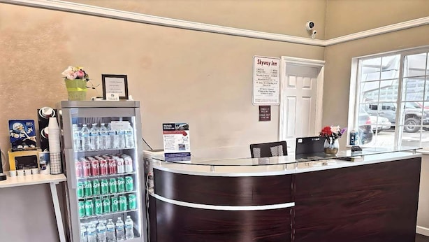 A reception desk with a refrigerator stocked with beverages, a sign for Skyway Inn, and a window with a view of parked cars.