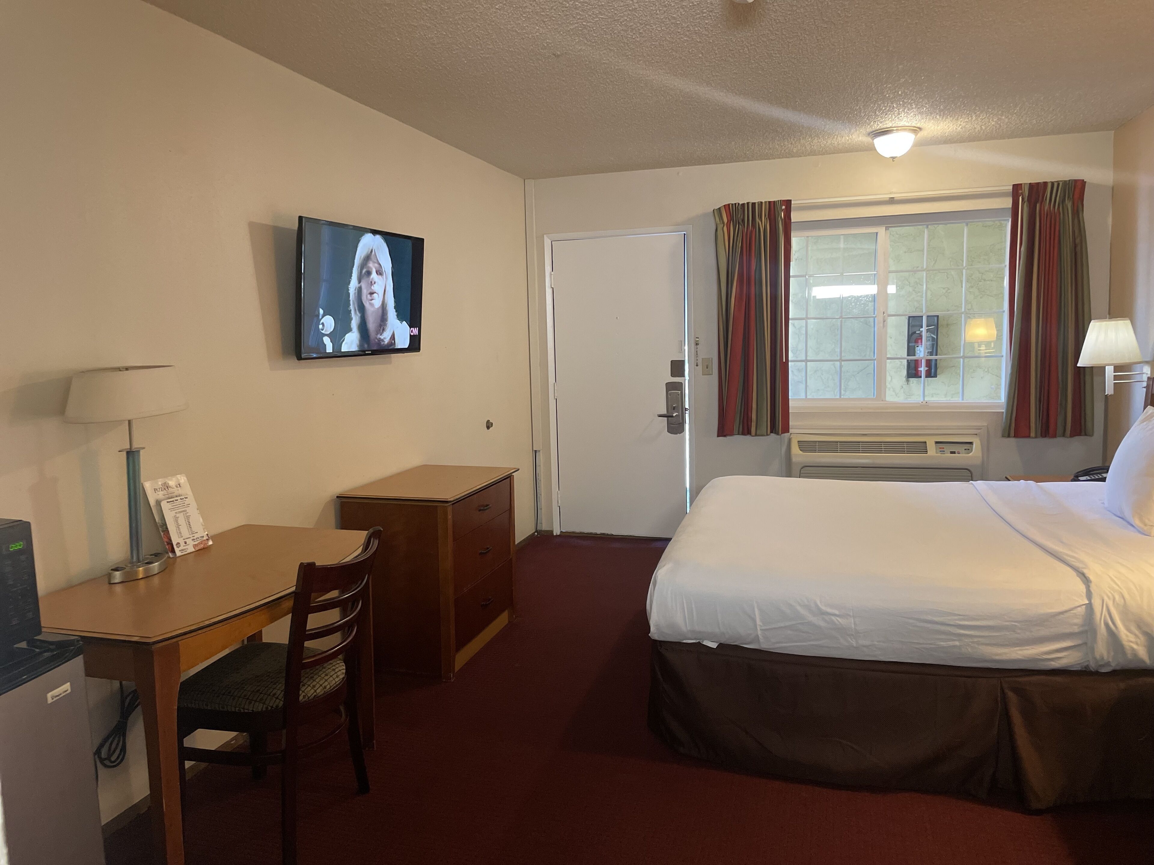 Une chambre d’hôtel équipée d’un lit, d’un bureau, d’une chaise, d’une télévision et d’une fenêtre avec des rideaux.
