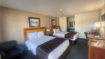 A hotel room with two beds, a desk, a chair, and a small kitchenette.