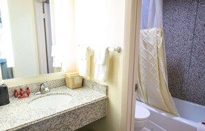 Une salle de bain avec un lavabo en granit, des serviettes blanches, des toilettes et un rideau de douche.