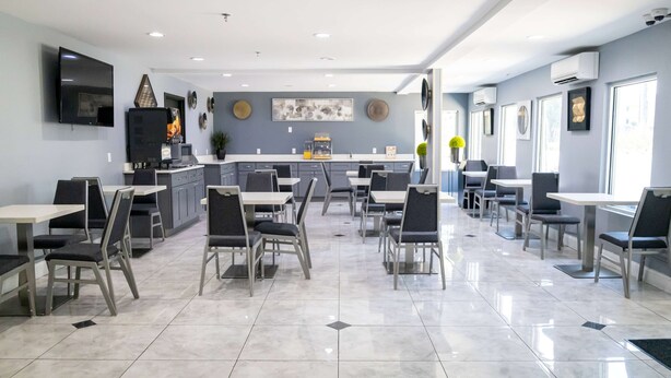 Un comedor moderno con cocina a la vista, que incluye un televisor de pantalla plana, una cafetera y diversas opciones de asiento.