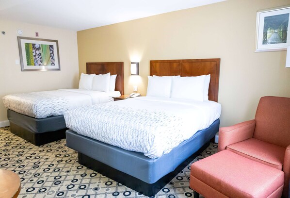 A hotel room with two beds, a red armchair, and a patterned floor.