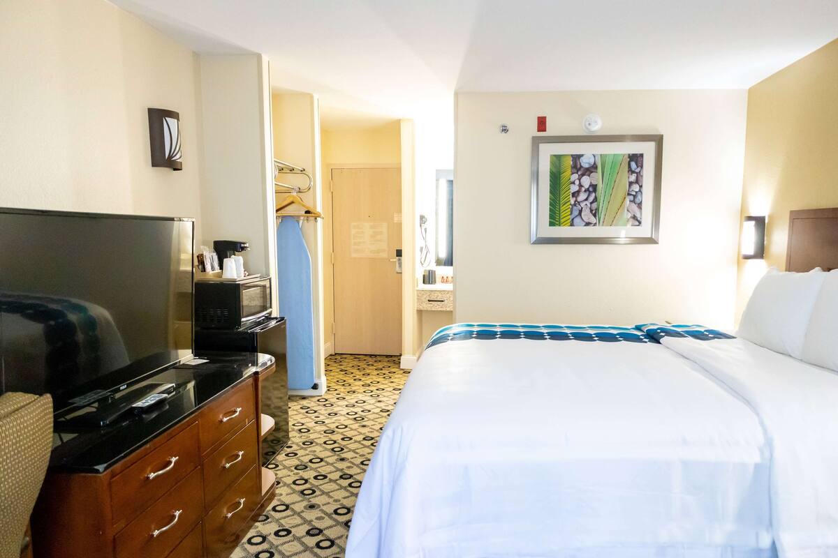 Habitación de hotel con una cama, televisor, cómoda y baño visible a través de una puerta abierta.