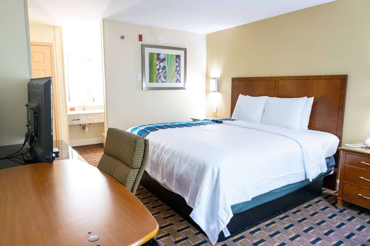 Habitación de hotel con cama, escritorio, silla, televisor y un cuadro en la pared.