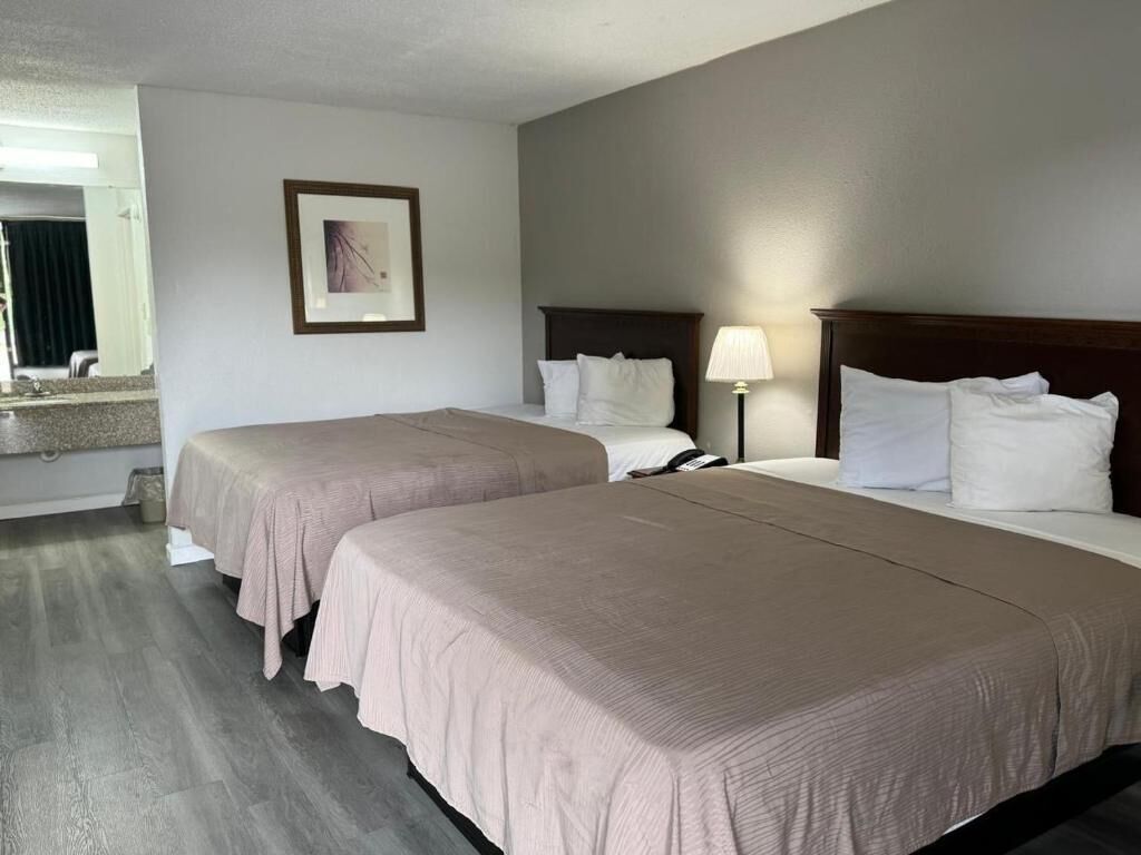 A hotel room with two beds, a bedside lamp, a framed picture on the wall, and a mirror.