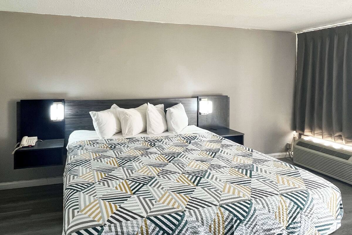 A hotel room with a bed, a nightstand, a phone, and a window with curtains.