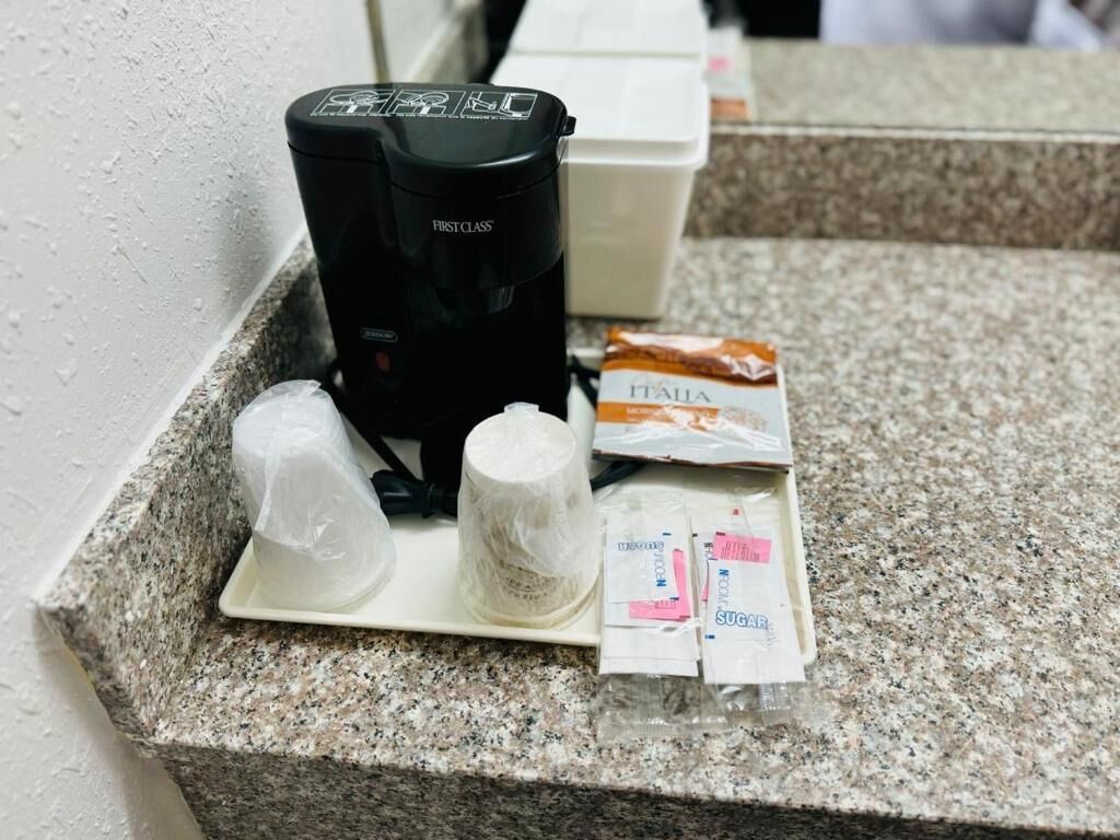A countertop with a coffee maker, a roll of toilet paper, and packets of sugar and tissues.