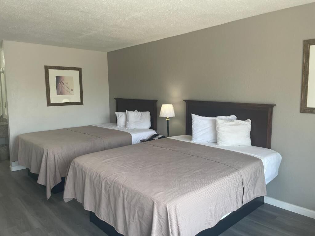 A hotel room with two beds, a nightstand, a lamp, and a framed picture on the wall.