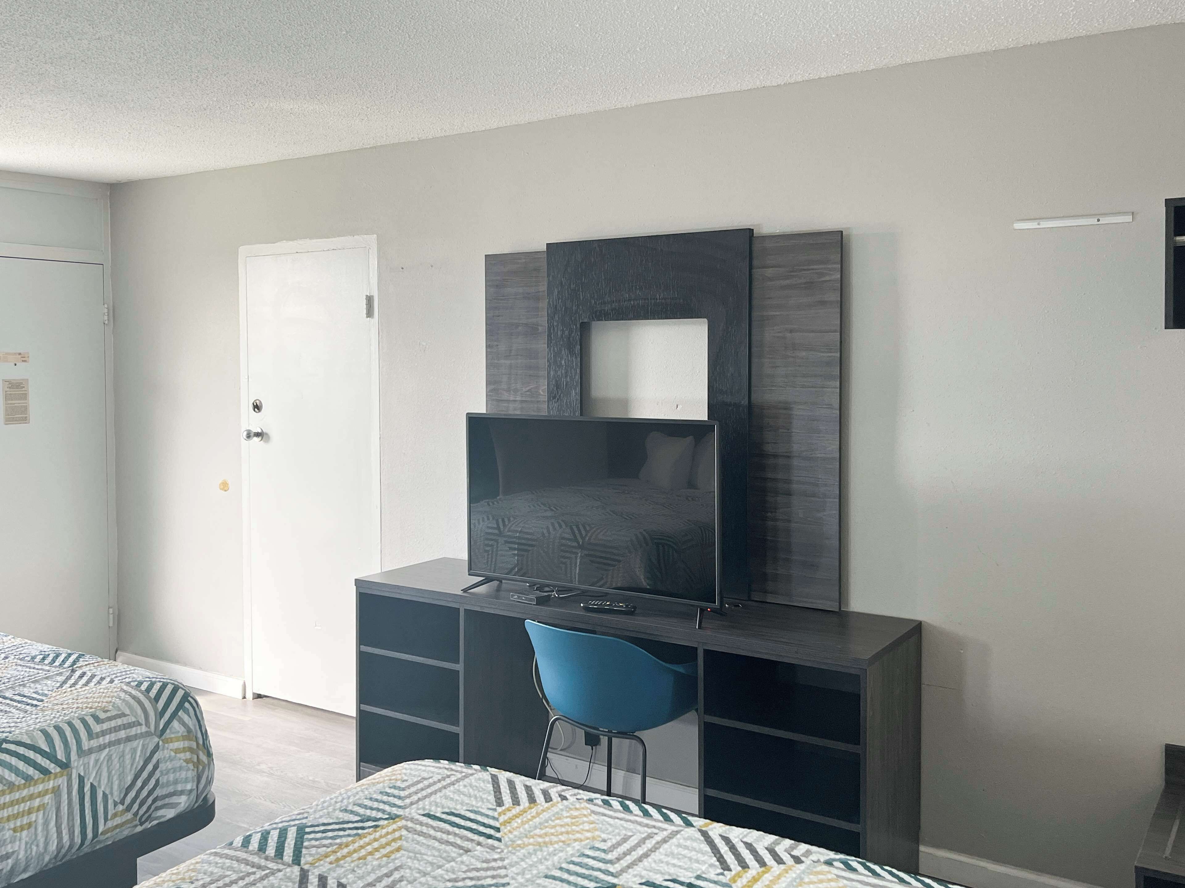 Una habitación moderna con una cama, un escritorio con una silla y un televisor montado en la pared.