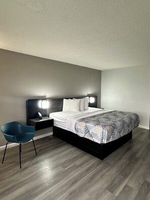 Un dormitorio moderno con una cama grande, una mesita de noche, una silla azul y una lámpara de pared.