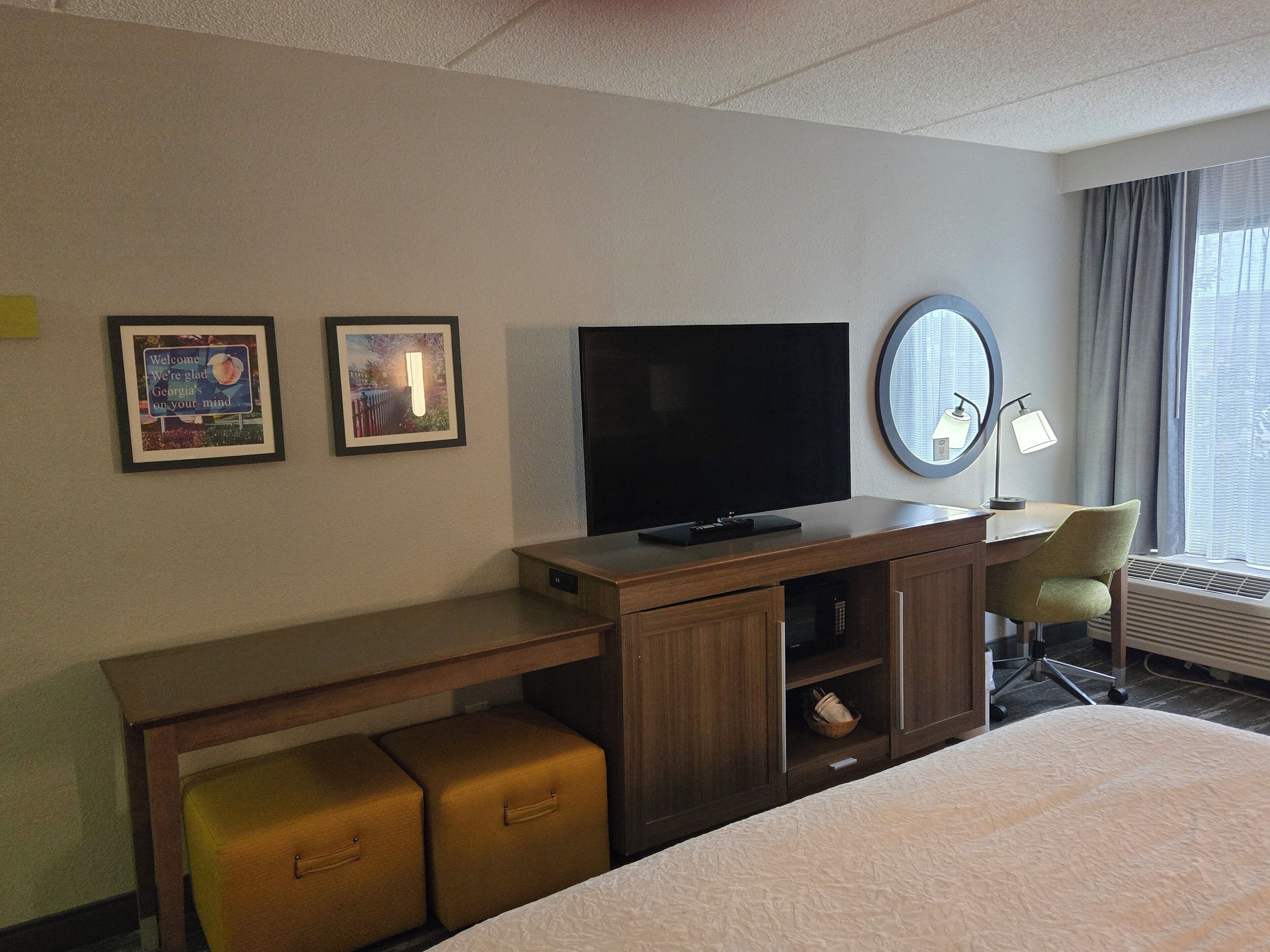 Habitación de hotel con televisión de pantalla plana, escritorio con lámpara, una silla y una cama.