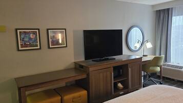 Habitación de hotel con televisión de pantalla plana, escritorio con lámpara, una silla y una cama.