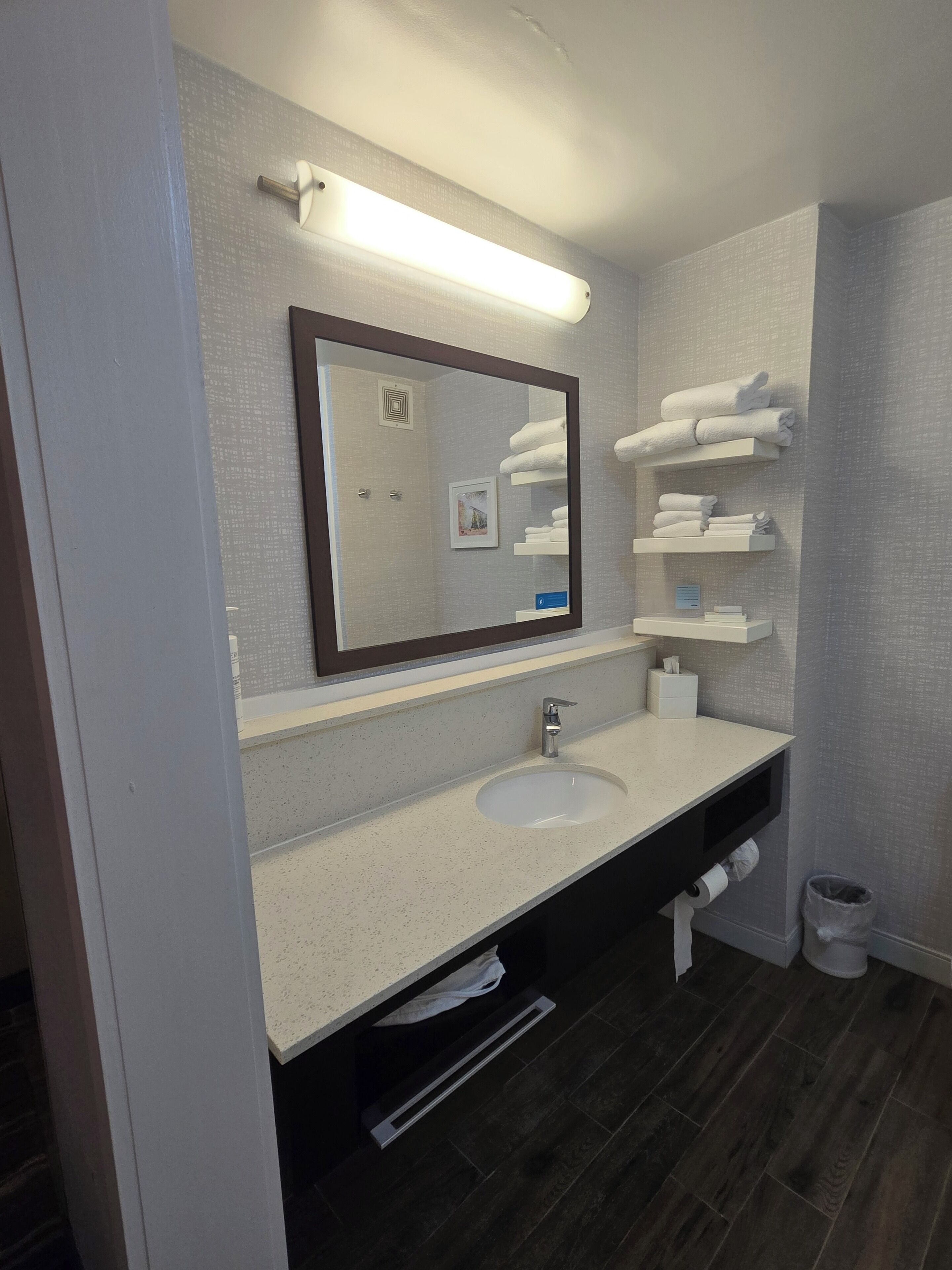 Un baño moderno con un espejo grande, un lavamanos, toalleros y un dispensador de papel higiénico.