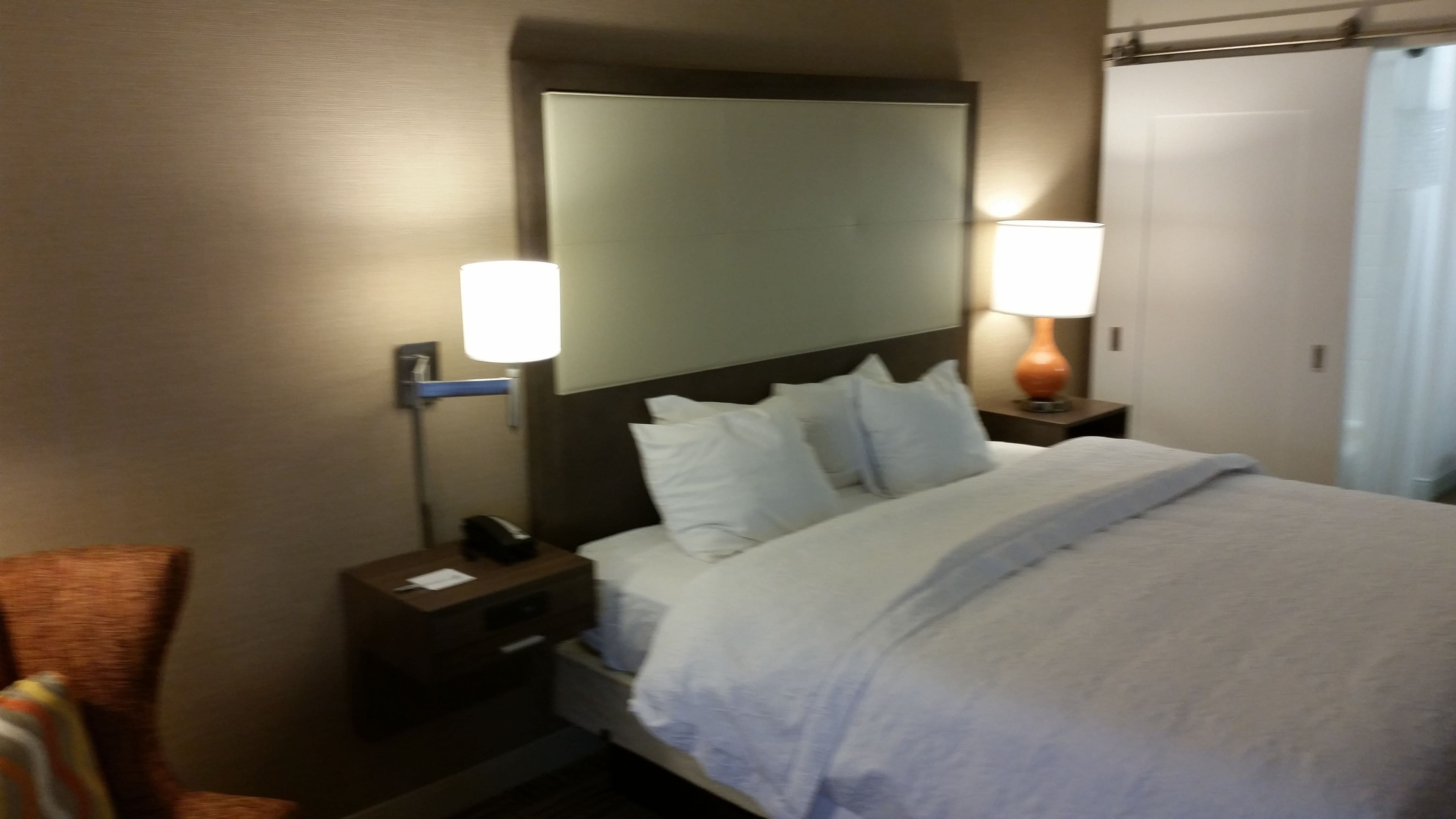A hotel room with a bed, two bedside tables, a nightstand, a mirror, and a lamp.