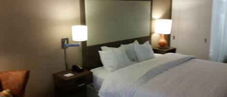 A hotel room with a bed, two bedside tables, a nightstand, a mirror, and a lamp.