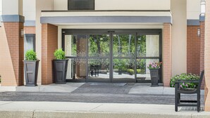 A hotel entrance with a glass door, potted plants, and a bench. - Hampton Inn Commerce (Commerce)
